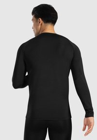 Schwarzes Langarm-Sportshirt mit enganliegender Passform, glatter Textur und Raglanärmeln, das einen minimalistischen Stil präsentiert.