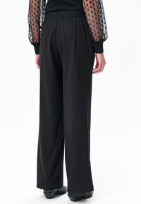 Zwarte wijde broek met elastische tailleband, met een gladde textuur. Kenmerken zijn onder andere een strakke snit en een ontspannen silhouet.