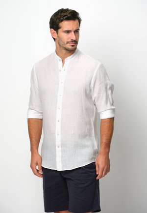 Weißes Leinenhemd mit Stehkragen, langen Ärmeln, die bis zu den Ellbogen gerollt sind, und einer Knopfleiste, kombiniert mit navy Shorts.