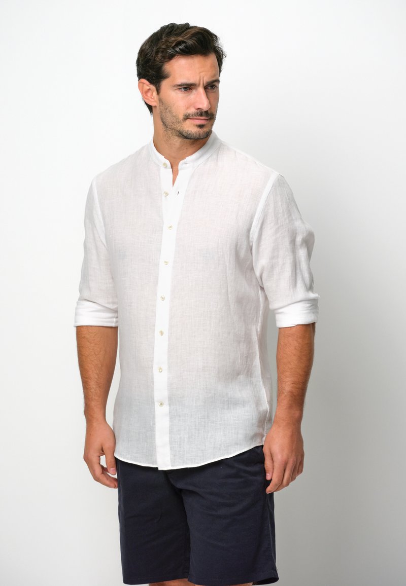 Witte linnen overhemden met een staande kraag, met lange mouwen opgerold tot de ellebogen en een knoopsluiting aan de voorkant, gecombineerd met navy shorts.