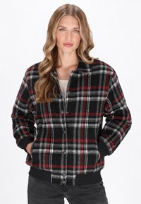 Veste à carreaux noire, rouge et grise, avec un devant boutonné, un col et des poignets élastiques, fabriquée dans un tissu texturé et dotée de deux poches latérales.