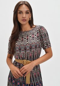 Sukienka z krótkim rękawem z wielokolorowym wzorem piór z czarnymi, kremowymi, czerwonymi i niebieskimi akcentami, wcięta w talii z beżowym paskiem.