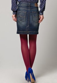 Falda de mezclilla con un tono oscuro, corte recto y bolsillos traseros visibles. Combinada con medias burdeos y zapatos de tacón altos azules.