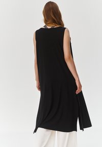 Czarna sukienka bez rękawów o luźnym kroju, z okrągłym dekoltem i bocznymi rozcięciami; wykonana z lekkiego, gładkiego materiału.