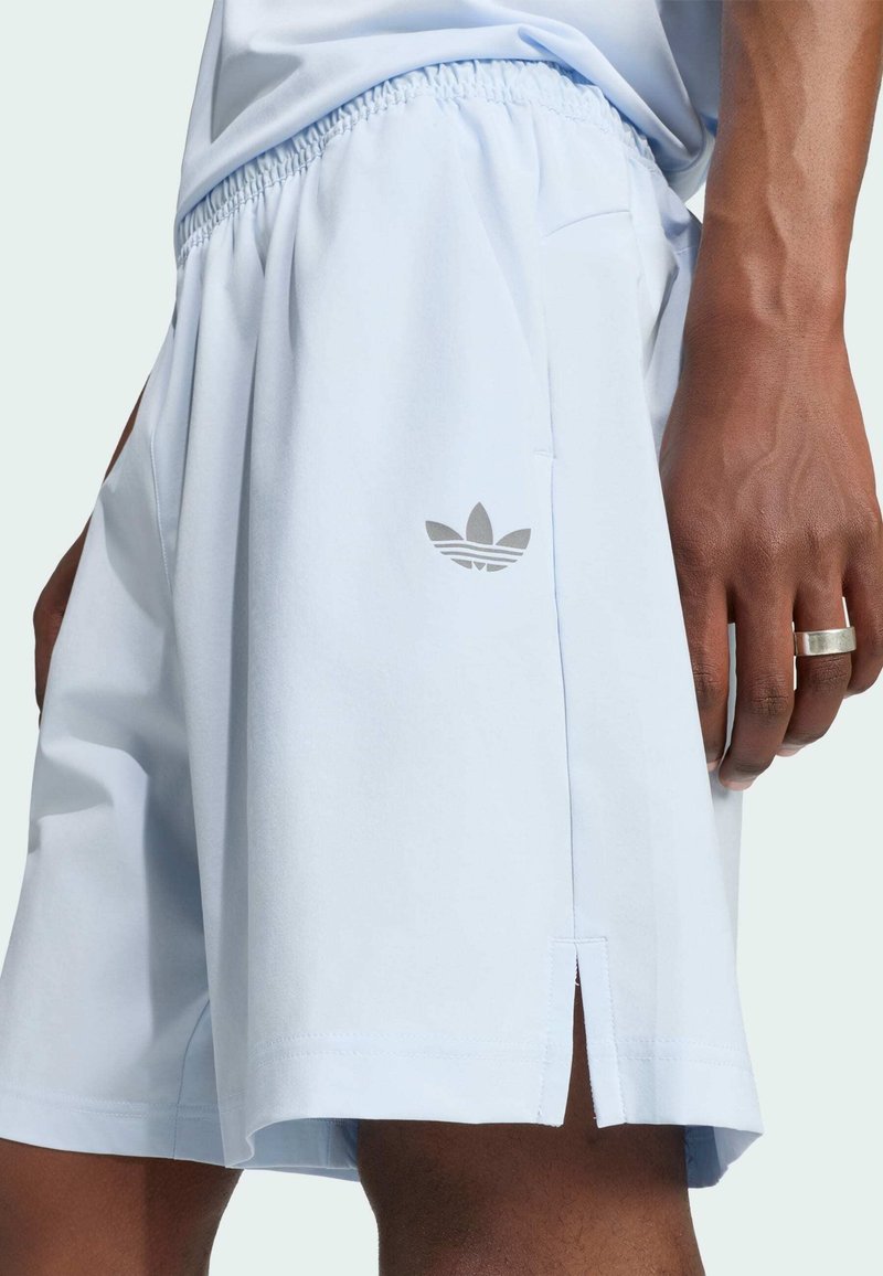 Primer plano de una persona que lleva pantalones cortos azul claro con una cintura elástica y un pequeño logo de Adidas cerca del dobladillo.