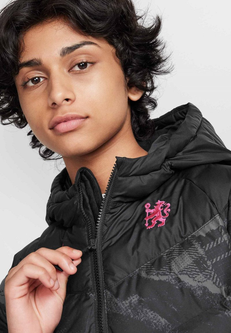 Chaqueta acolchada negra con capucha, que presenta un logo de león rosa y un patrón texturizado en un lado, cierre frontal con cremallera y una tela suave.