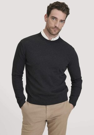 Dunkelgrauer Rundhals-Pullover aus glattem Strickstoff, mit langen Ärmeln sowie gerippten Bündchen und Saum, kombiniert mit beigen Hosen.