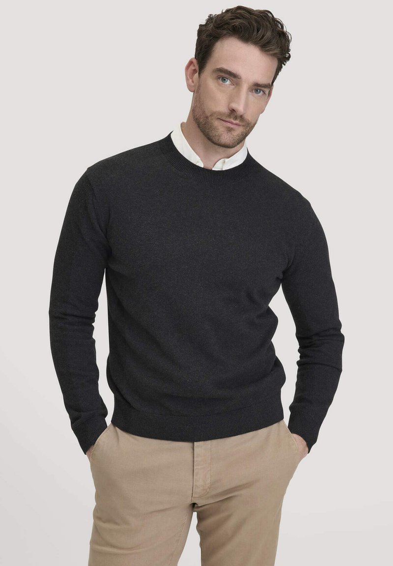 Dunkelgrauer Rundhals-Pullover aus glattem Strickstoff, mit langen Ärmeln sowie gerippten Bündchen und Saum, kombiniert mit beigen Hosen.