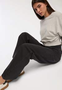 Felpa grigia abbinata a jeans neri morbidi. L'outfit presenta un design rilassato e una consistenza liscia, accentuato da sneaker bianche.