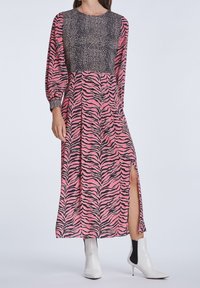 Langes Kleid mit rosa und schwarzen Zebra-Streifen, ausgestattet mit einem strukturierten schwarzen Oberteil und einem seitlichen Schlitz. Kombiniert mit weißen Knöchelstiefeln.