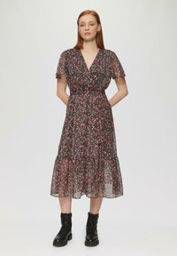Robe florale noire avec des manches courtes et transparentes, un décolleté en V, et une jupe à volants, associée à des bottines à lacets noires.