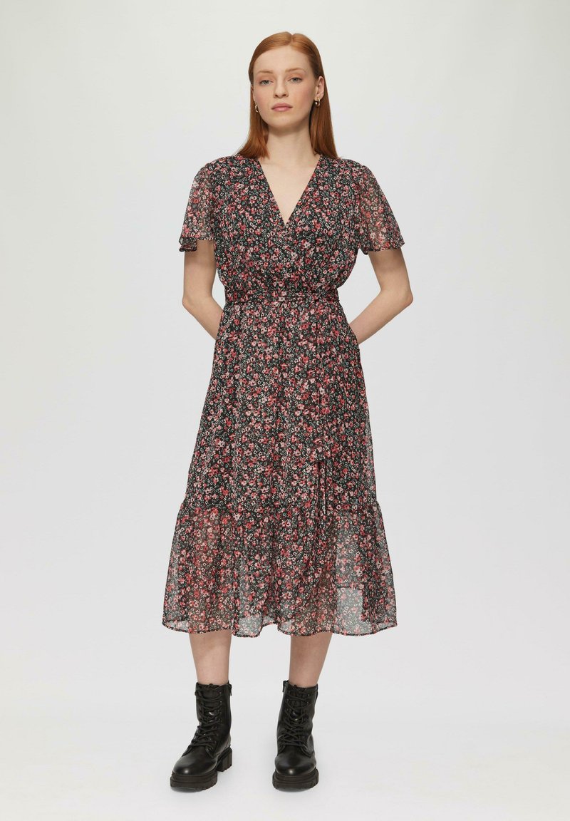Robe florale noire avec des manches courtes et transparentes, un décolleté en V, et une jupe à volants, associée à des bottines à lacets noires.