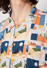 Chemise à manches courtes en coton avec un motif géométrique multicolore, dotée d'un col, de boutons en bois et d'une poche poitrine.