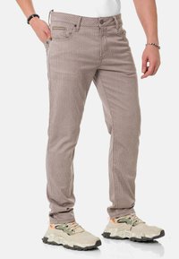 Hellbraune gestreifte Hosen in Slim-Fit mit Vordertaschen und Metallknopfverschluss, kombiniert mit beigen Sportschuhen.