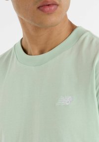 T-shirt di un tenero verde menta realizzata in morbido cotone. Presenta un collo rotondo e un piccolo logo ricamato in bianco sul petto.