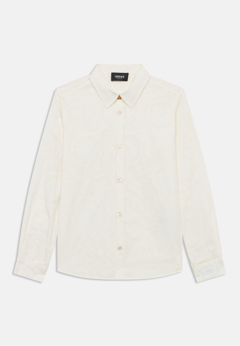 Λευκό πουκάμισο με μακριά μανίκια και κουμπιά, με λουλουδάτο σχέδιο, κλασικό γιακά, μεταλλικά στοιχεία σε χρυσό τόνο και ευθεία γραμμή στο τελείωμα. Ορατή ετικέτα με το εμπορικό σήμα.