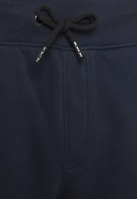 Mørkeblå joggebukser med ribbestrikket midje, justerbar svart snor og en frontlomme med et subtilt sømmønster.