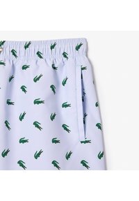 Pantaloni da bagno azzurri chiari con vita elastica, decorati con un motivo ripetuto di coccodrilli verdi e una tasca laterale.