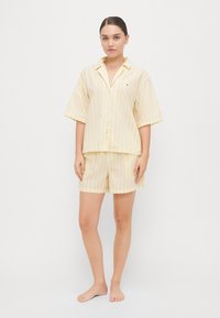 Gul og hvitstripet kortermet pysjamassett med knappesluss og matchende shorts, laget av lett stoff.