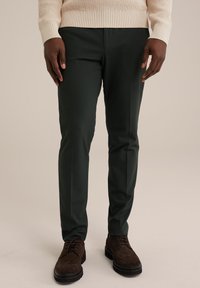 Pantaloni verzi închise cu o croială ajustată, confecționați dintr-un material neted. Purtați cu pantofi din suede maro, având un pulover tricotat texturat deasupra.