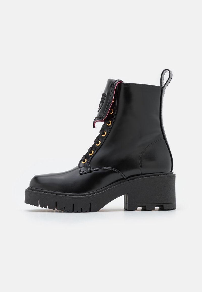 Schwarzer Leder-Stiefelette mit goldfarbenen Ösen, dicker Plateau-Sohle und einem umgeschlagenen Klappdetail. Verfügt über eine Zuglasche an der Ferse für leichteres Anziehen.