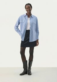 Blue and white striped shirt with two front pockets, paired with a black corduroy skirt and knee-high black boots. Smooth texture.