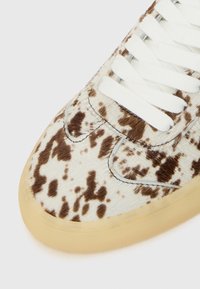 Brun og hvit prikkete kueskinn sneakers med flate hvite snører og en gjennomsiktig gummisåle. Strukturert overflate med detaljerte sømmer.