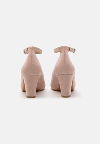 Scarpe beige in suede con tacco a blocco, cinturino alla caviglia posteriore e punta arrotondata. Texture liscia e tacco robusto, progettate per garantire stabilità.