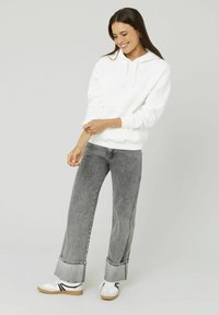 Sweatshirt à capuche blanche avec une poche kangourou, porté avec un jean large gris taille haute et des baskets blanches avec des accents noirs.