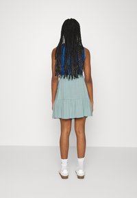 Hihaton mekko, jossa on sininen yläosa ja vaaleanvihreä hulmuava hame, joka on varustettu röyhelöreunalla. Yhdistetty valkoisten sukkien ja rentojen kenkien kanssa.