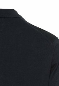 Czarna koszulka polo z teksturowanej tkaniny, z prążkowanym kołnierzykiem i lekko usztywnionymi szwami na ramionach. Prosty i uniwersalny design.