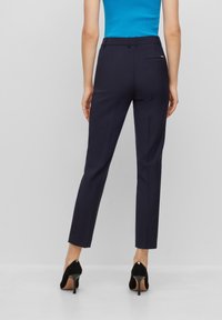 Pantalones de corte entallado en color navy, con una textura suave, trabillas para el cinturón y un bolsillo trasero. Combinados con zapatos de tacón alto negros.