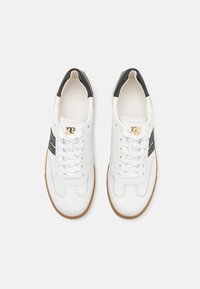 Baskets en cuir blanc avec un accent noir, dotées de lacets blancs, d'une surface texturée et d'une semelle en caoutchouc naturel. Détail du logo doré sur la languette.