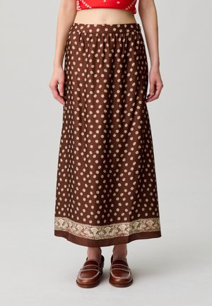 Gonna midi marrone con piccolo motivo floreale bianco e bordo decorativo, indossata con mocassini marroni e top corto rosso.