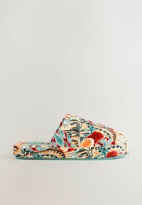 Lukket hjemmesko med livlige abstrakte blomster mønstre i rødt, blågrønt, orange og brunt på en lys baggrund, set fra siden på en ensfarvet overflade.