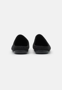 Black slip-on shoes with a soft fabric upper and a rounded toe. Textured details around the opening and a smooth rubber sole.