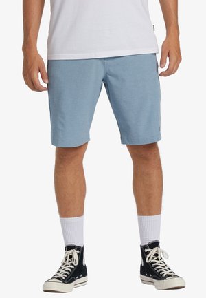 Lys blå shorts lavet af et blødt stof, med en afslappet pasform og let opfoldet kant. Sammen med sorte højhælede sneakers og hvide sokker.
