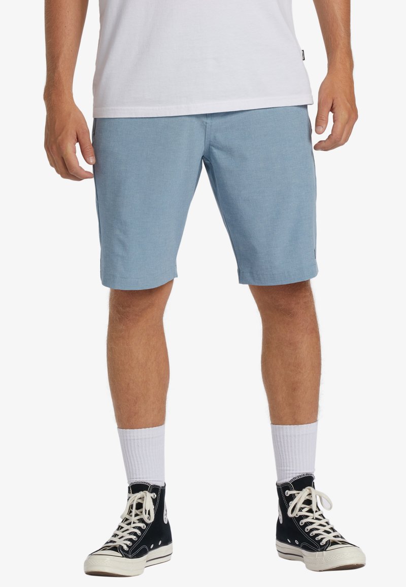 Light blue shorts made of a soft fabric, featuring a relaxed fit and slightly rolled hem. Paired with black high-top sneakers and white socks.
