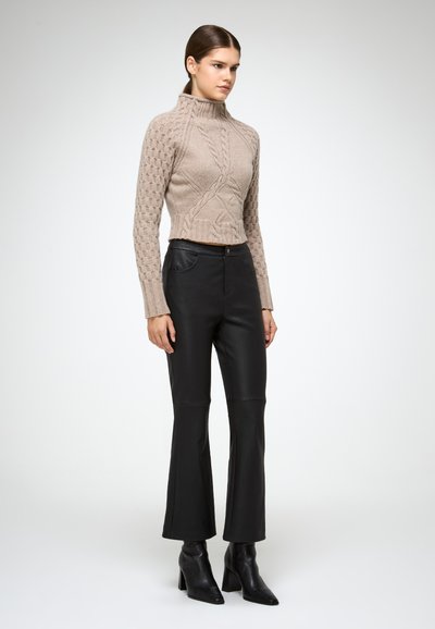 Suéter corto de punto beige con cuello alto y patrón texturizado, combinado con pantalones de imitacion de cuero negros acampanados y botas negras de puntera.