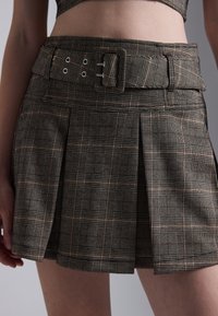 Plaid mini skirt in dark tones with a structured belt featuring metal hardware. Contains pleats and a textured fabric pattern.