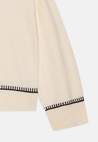 Cremfarbener Sweaterärmel mit gerippten Bündchen, der ein kontrastierendes schwarzes Stickmuster am Saum für zusätzliche Details aufweist.