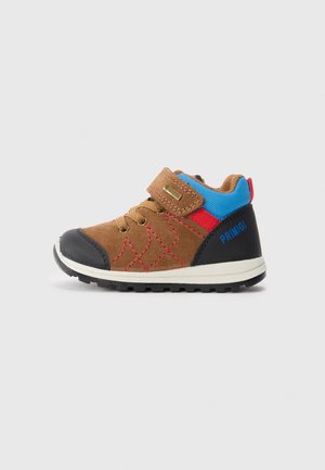 Chaussure pour tout-petits en suède marron et en caoutchouc noir avec des accents bleus et rouges, design à lacets et bande Velcro. Tige texturée avec un motif en losanges.