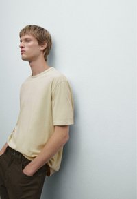 Maglietta beige a maniche corte in vestibilità rilassata, realizzata in tessuto morbido, abbinata a pantaloni marroni scuri. Design semplice con scollo rotondo.