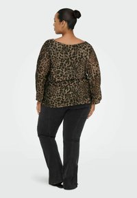 Top trasparente marrone con macchie leopardate nere, maniche lunghe e scollatura ampia abbinato a jeans grigi scuri attillati.