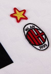 Wit sporttrui met een geborduurde rode ster en het AC Milan-logo, dat rode en zwarte strepen heeft met het jaartal "1899" eronder.