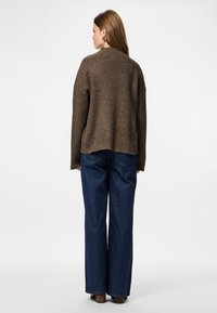 Femme de dos, vêtue d'un pull côtelé marron, d'un jean large bleu foncé et de chaussures à talons marron.