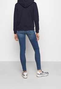 Felpa con cappuccio blu navy, jeans azzurri aderenti e sneaker sportive. I jeans hanno tasche posteriori e una vestibilità slim. Le sneaker presentano un design testurizzato multicolore.