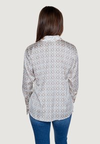 Chemise boutonnée avec un motif géométrique crème et marron, manches longues, col et ourlet arrondi. Fabriquée en tissu léger.