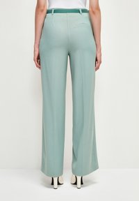 Široké kalhoty z měkké tkaniny v jemně mátové zelené barvě, s hladkým povrchem, poutky na opasek a jednou zadní kapsou.
