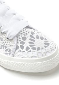 White sneaker featuring a lace mesh upper with geometric cutouts, flat laces, and a textured rubber sole. Lightweight and breathable design.
